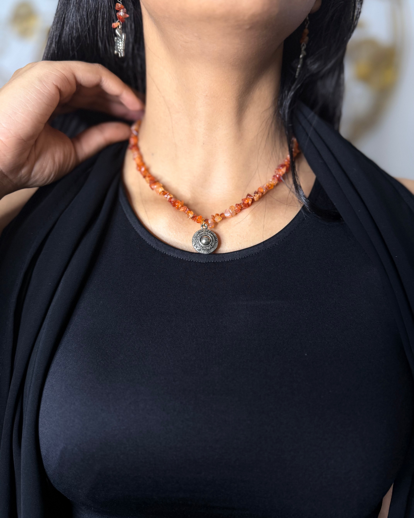 Person wearing a black top and orange beaded necklace with a pendant.