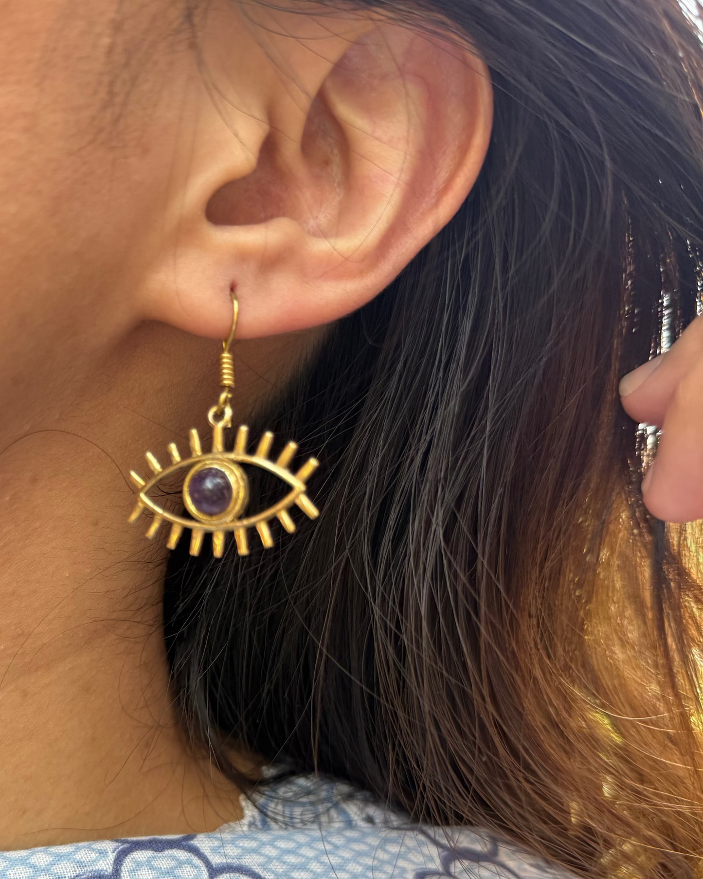 Close-up of a person wearing gold eye-shaped earrings with a blue floral patterned garment.