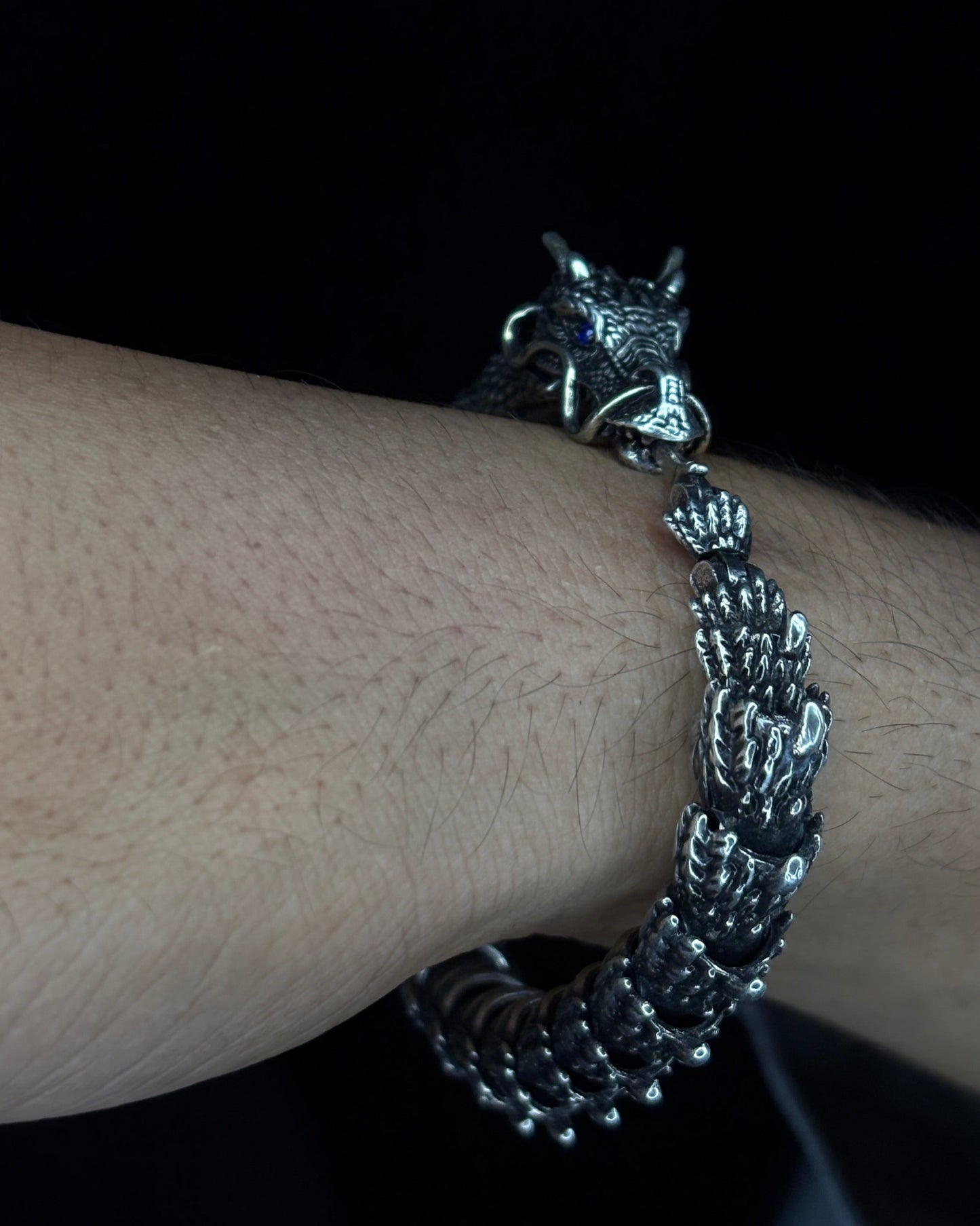 Silver bracelet with dragon charm on a wrist against a dark background
