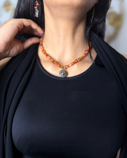 Person wearing a black top and orange beaded necklace with a pendant.