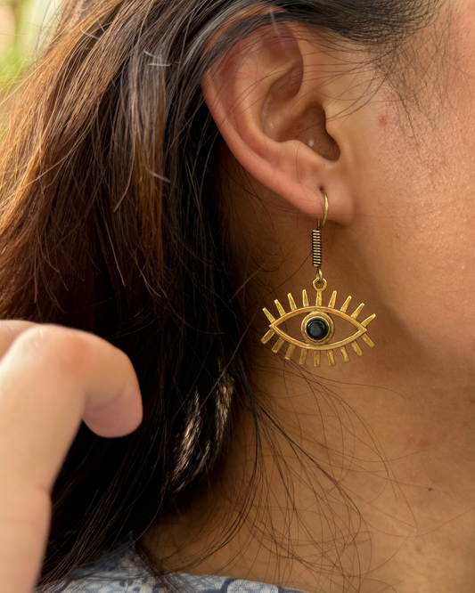 Gold eye-shaped earring with a black gemstone worn by a person.