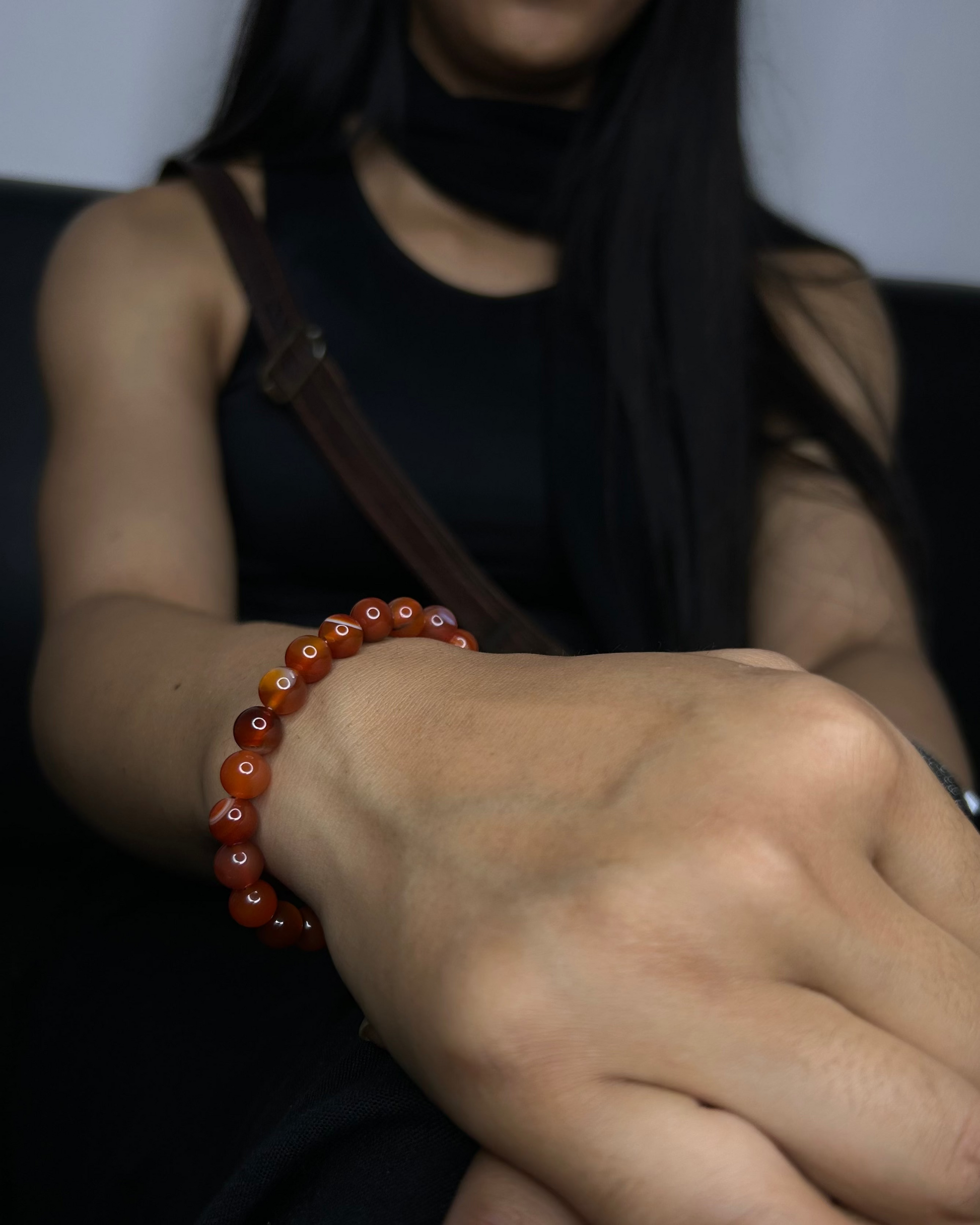 Close-up of a hand wearing a red beaded bracelet with a blurred background