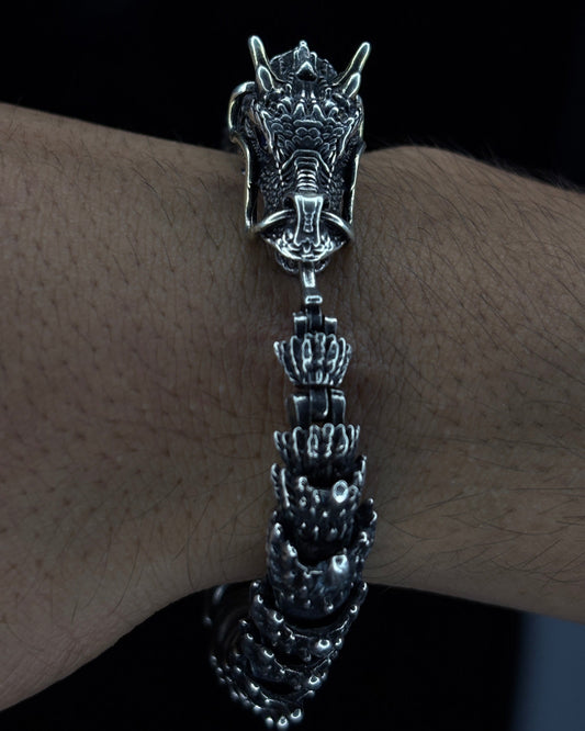 Silver bracelet with dragon design on a wrist against a dark background