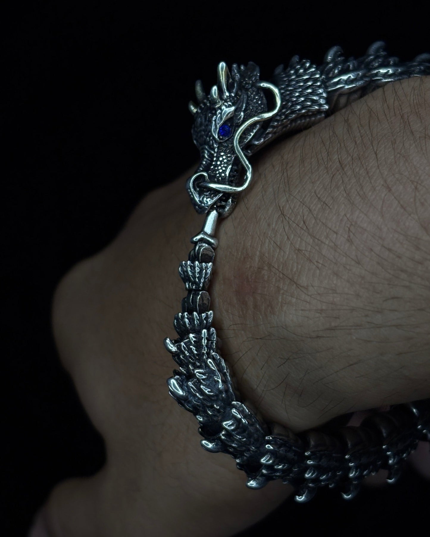Silver bracelet with dragon design on a wrist against a dark background