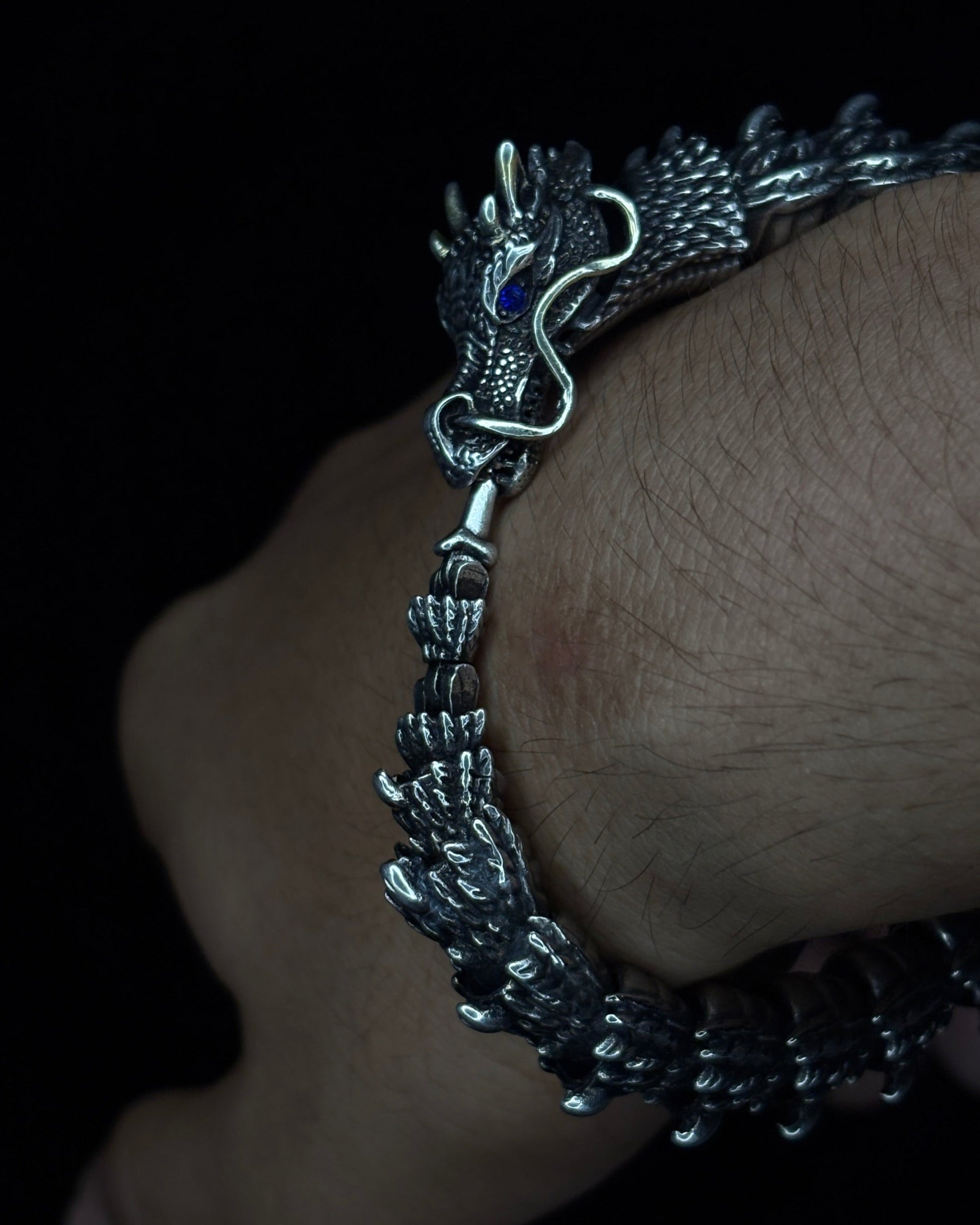 Silver bracelet with dragon design on a wrist against a dark background