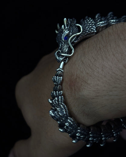 Silver bracelet with dragon design on a wrist against a dark background