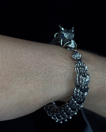 Silver bracelet with dragon charm on a wrist against a dark background